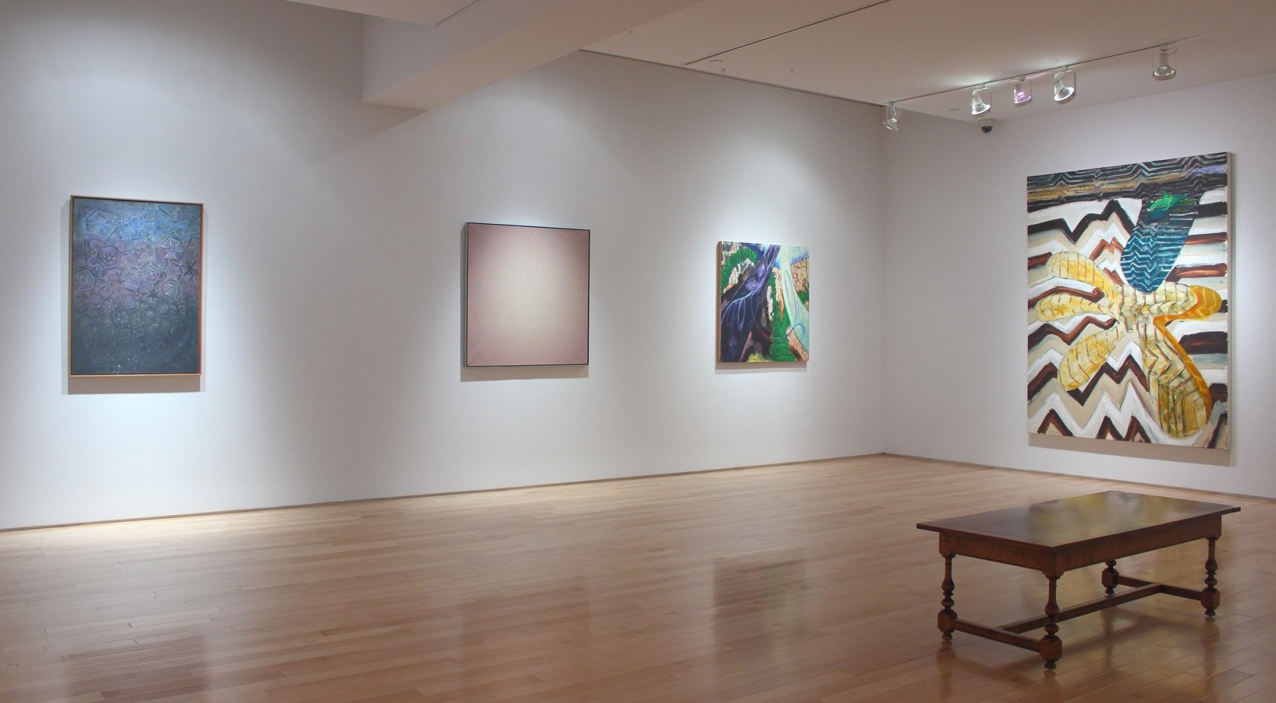 Photograph showing a corner view of an exhibition space, with on large painting and three smaller paintings hanging on white walls