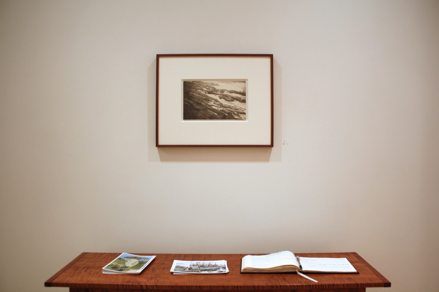 Photograph showing a view of an exhibition, with one small framed drawing hanging over a wooden table