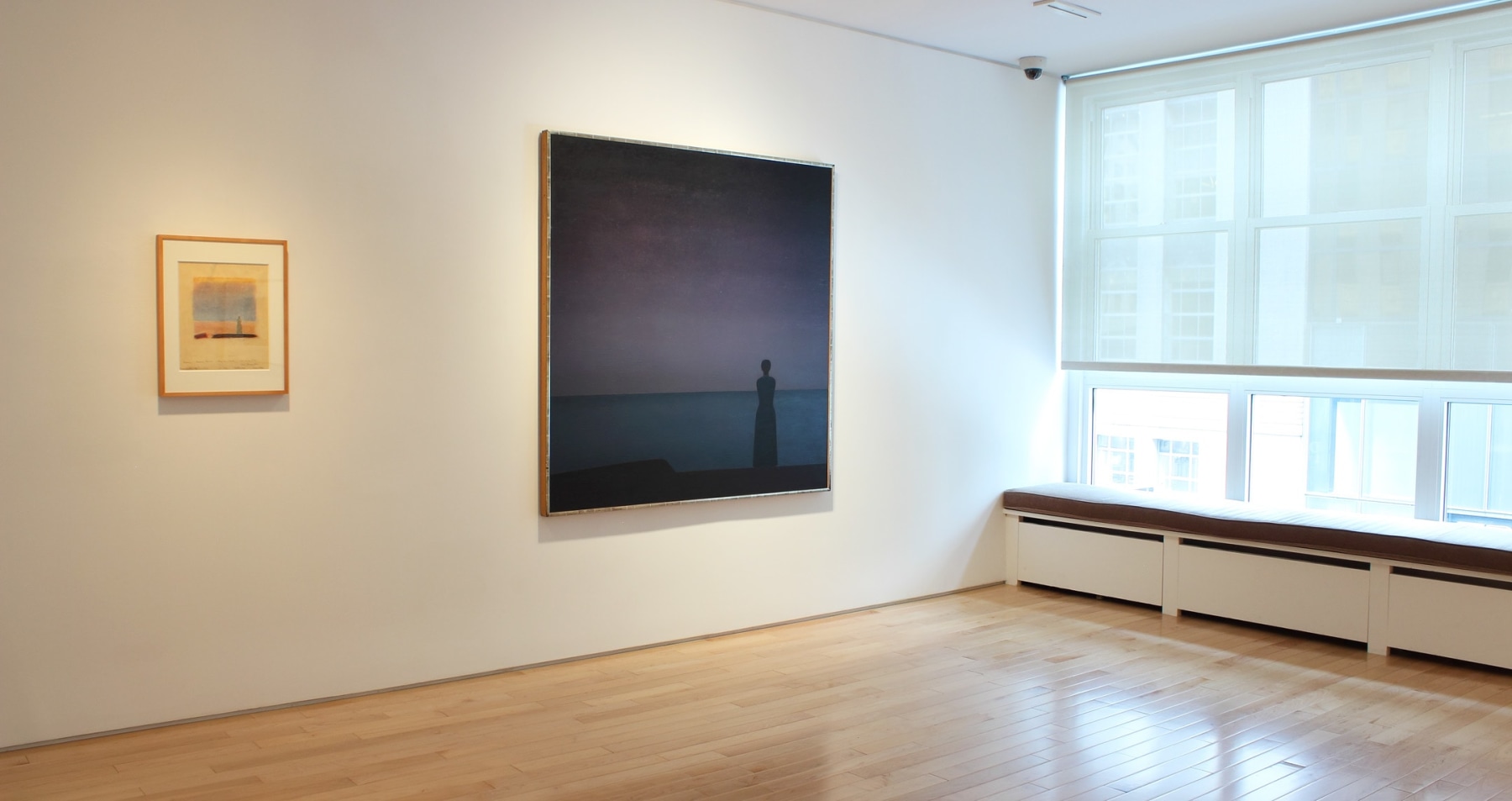 Photograph showing a view of an exhibition space, with two paintings hanging on a white wall