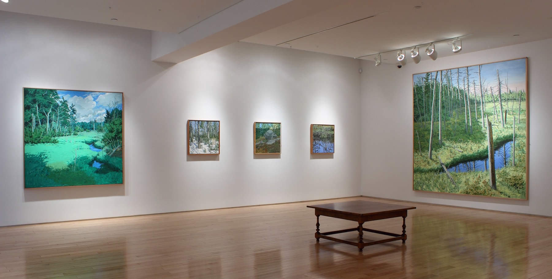 Photograph showing a corner view of an exhibition space, with five paintings hanging on white walls
