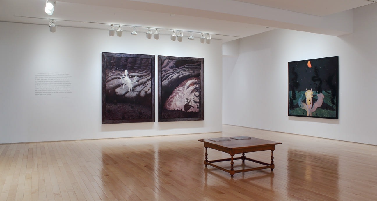 Photograph showing a corner view of an exhibition space with three paintings hanging on white walls