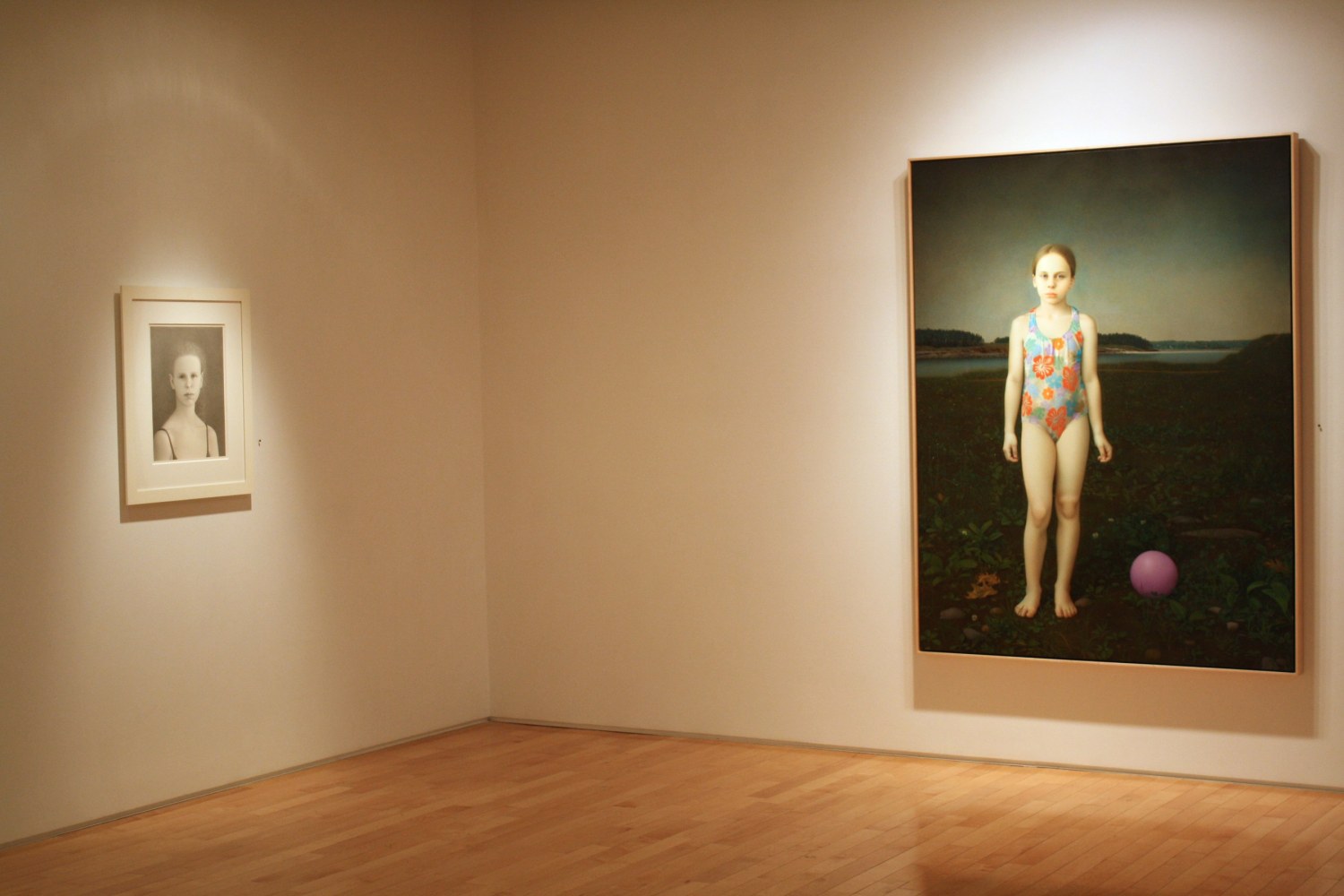 Photograph showing a corner view of an exhibition space, with one large framed painting and one small framed drawing hanging on white walls
