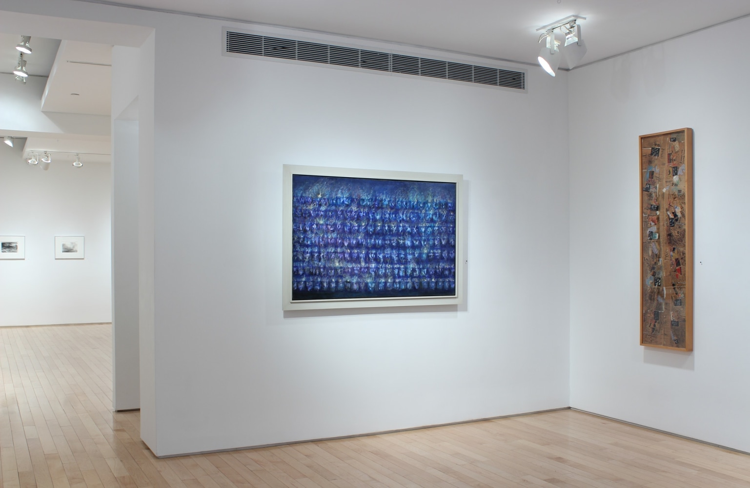 Photograph showing a corner view of an exhibition space, with two paintings hanging on white walls