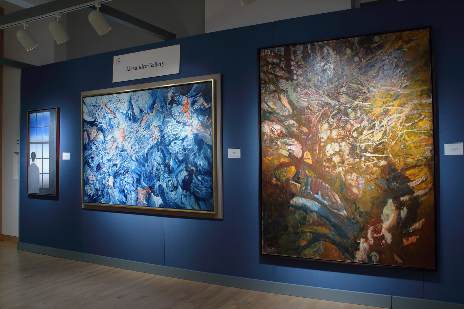 Photograph showing a view of an exhibition booth, with three paintings hanging on a blue wall