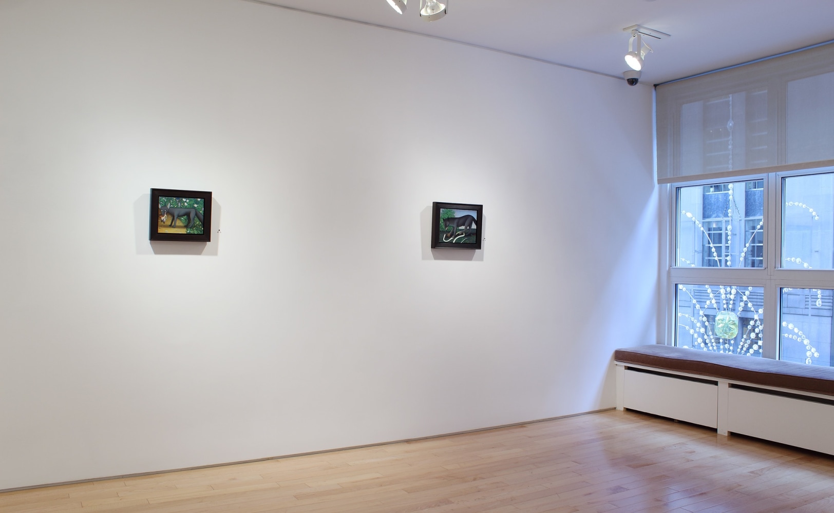 Photograph showing a view of an exhibition with two small paintings hanging on a white wall