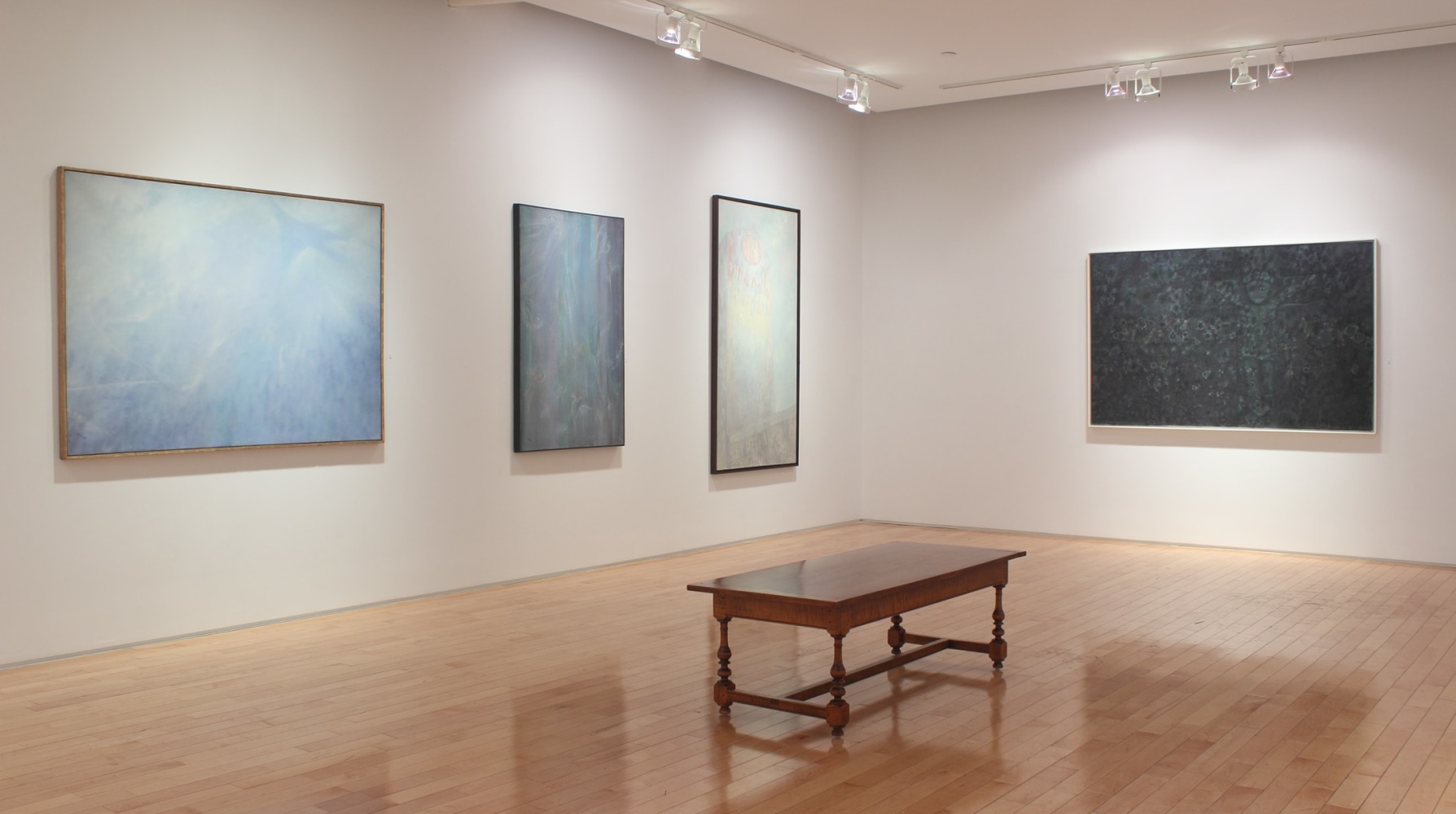 Photograph showing a corner view of an exhibition space, with four large paintings hanging on white walls
