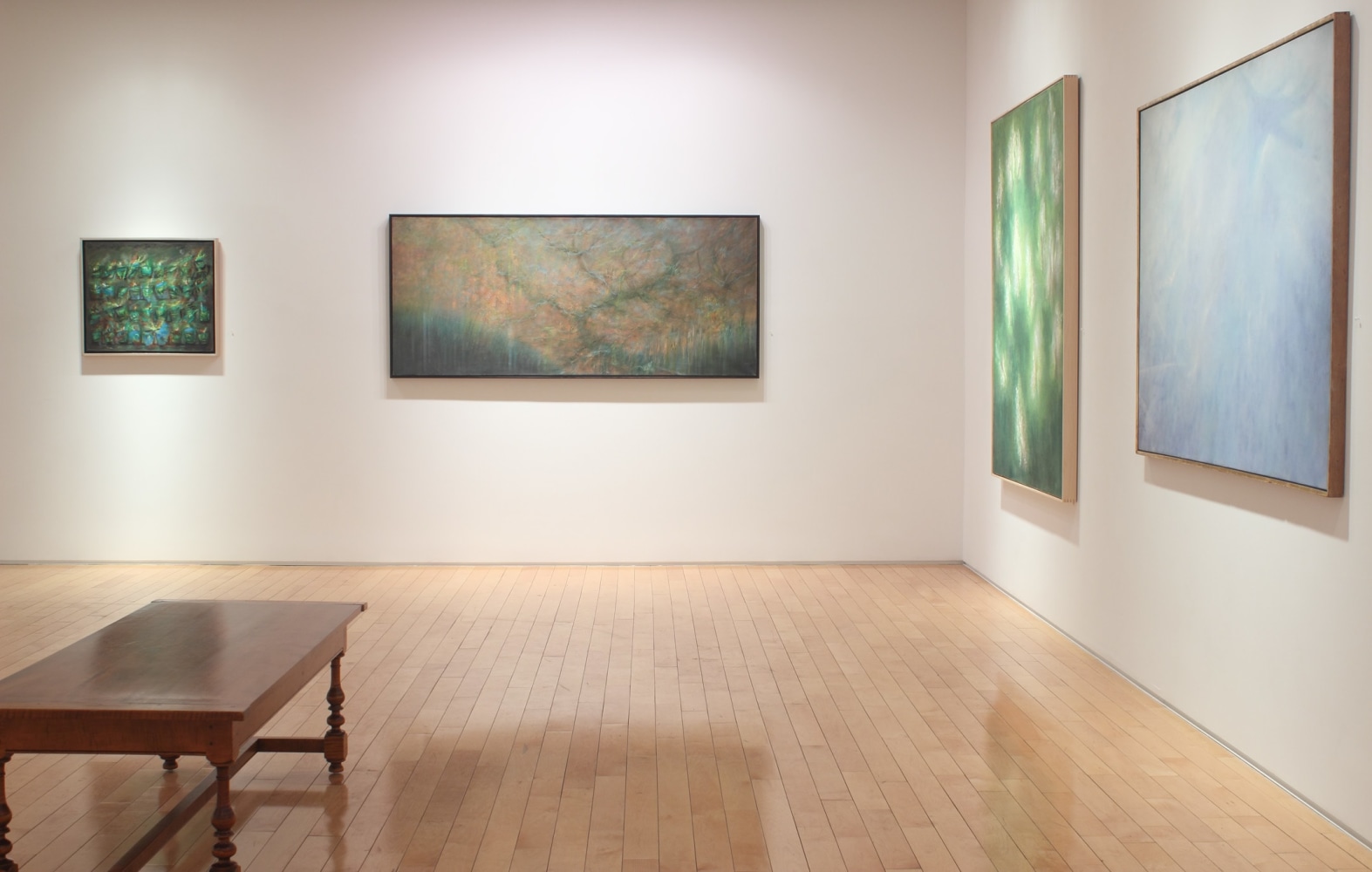 Photograph showing a corner view of an exhibition space with four painting hanging on a white wall