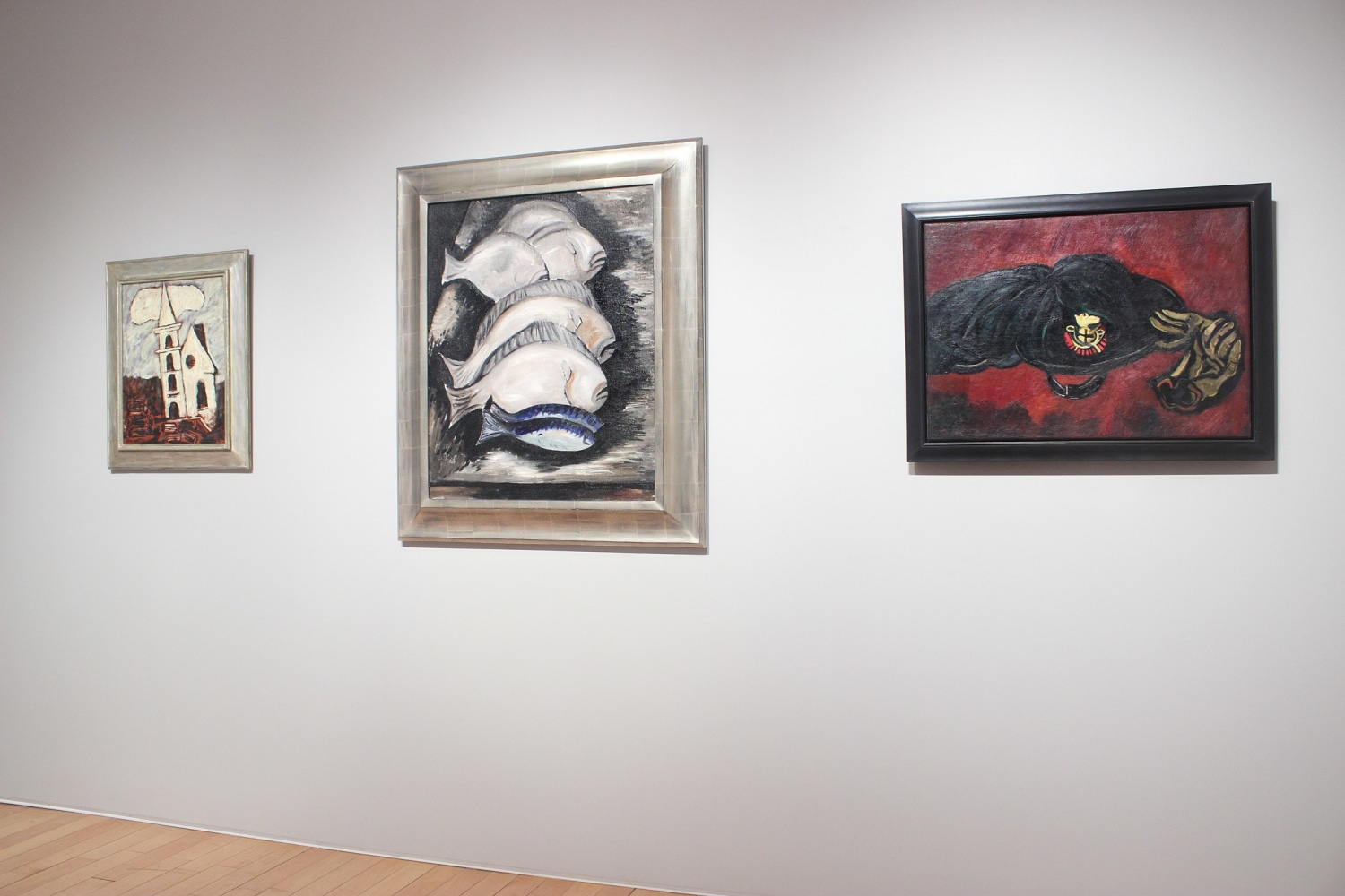 Photograph showing a view of an exhibition space, with three paintings hanging on a white wall
