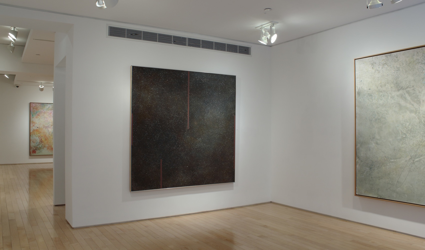 Photograph showing a view of an exhibition space, with three paintings hung on white walls