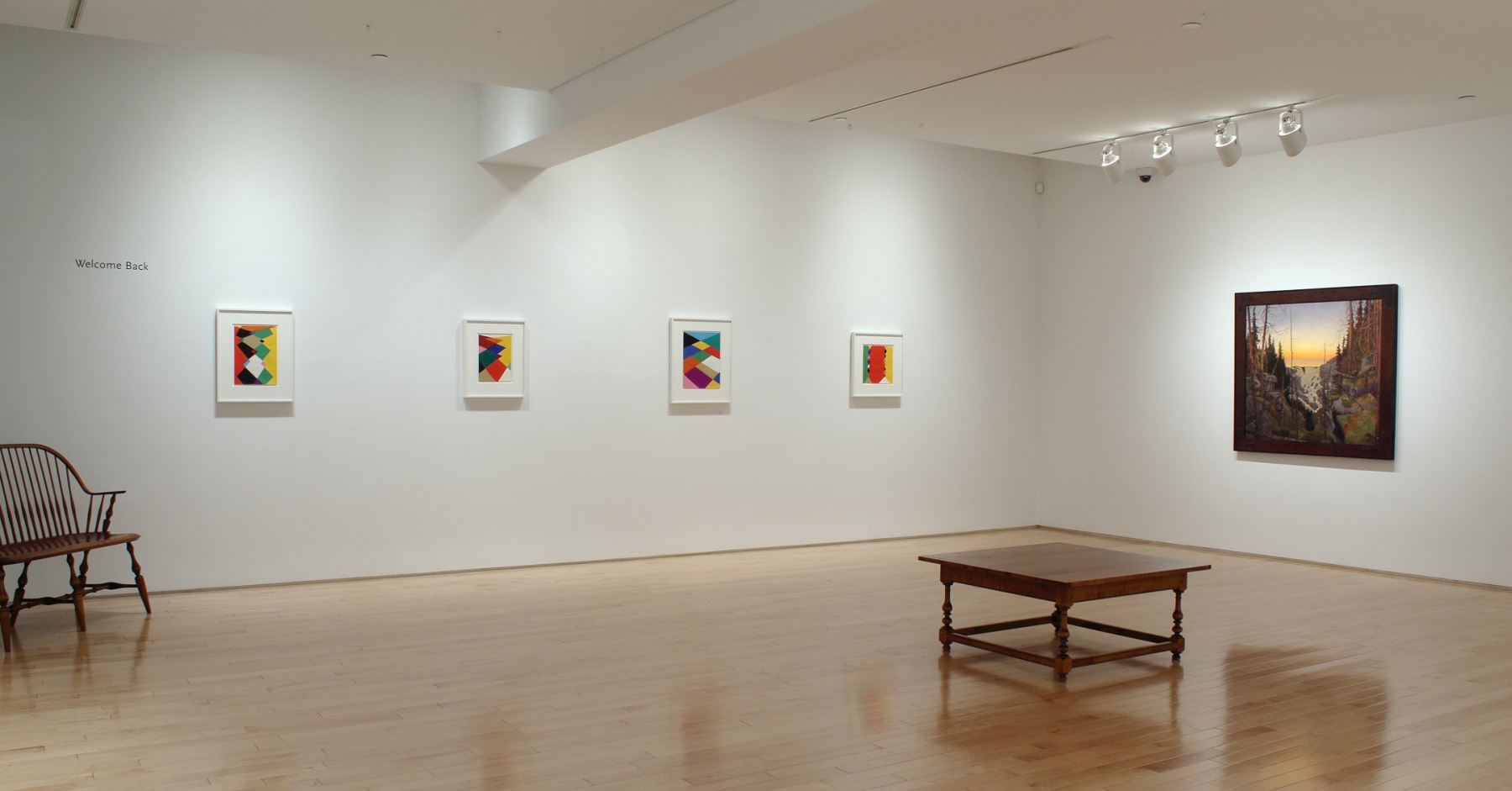 Photograph showing a corner view of an exhibition space, with five paintings hung on white walls