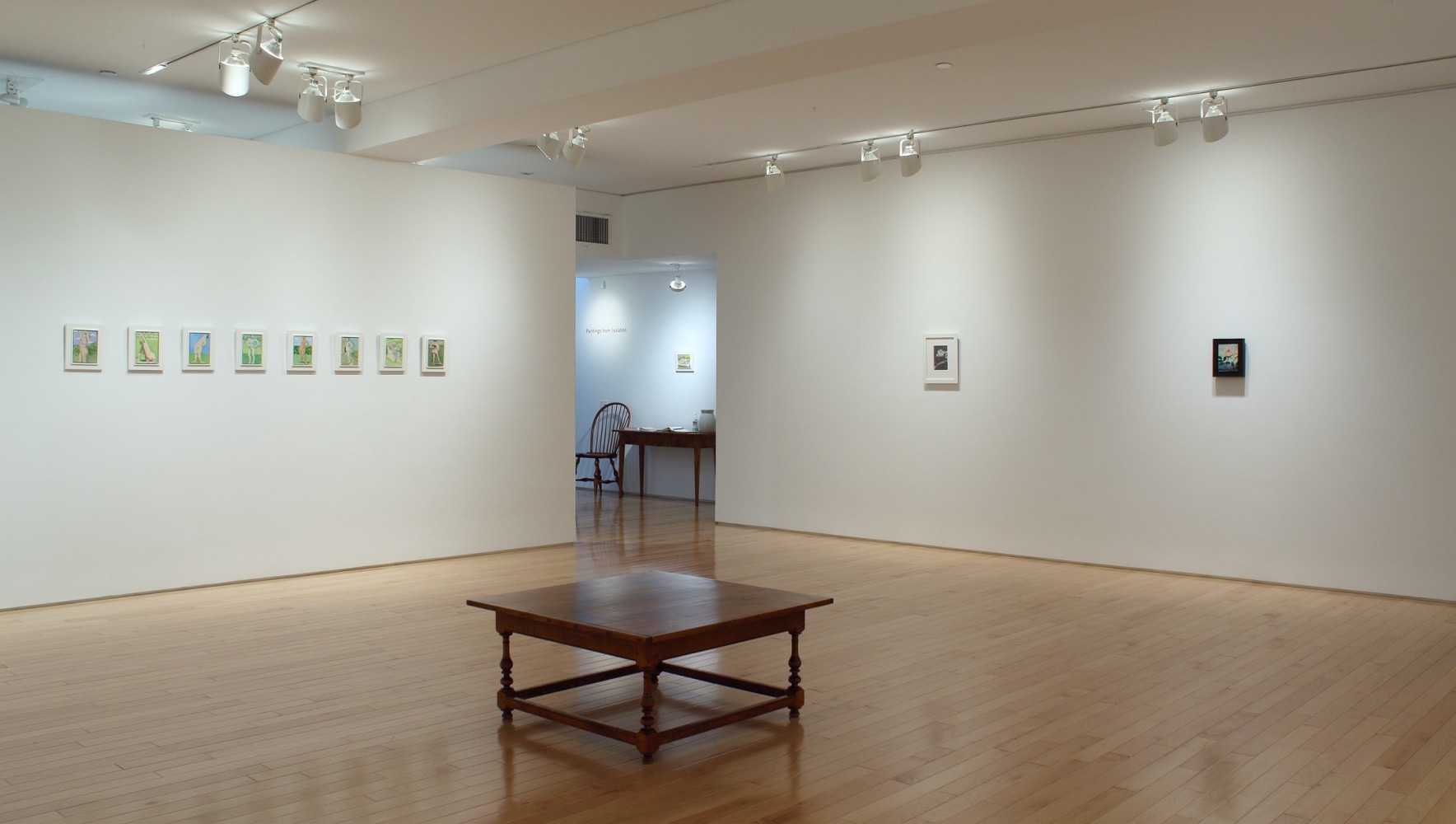 Photograph showing a corner view of an exhibition space, with eleven small paintings hung on white walls