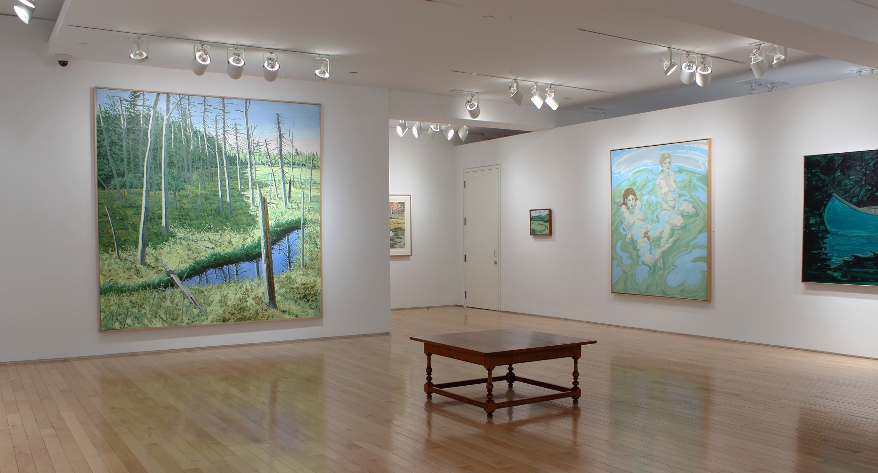 Photograph showing a corner view of an exhibition space with five paintings hanging on white walls
