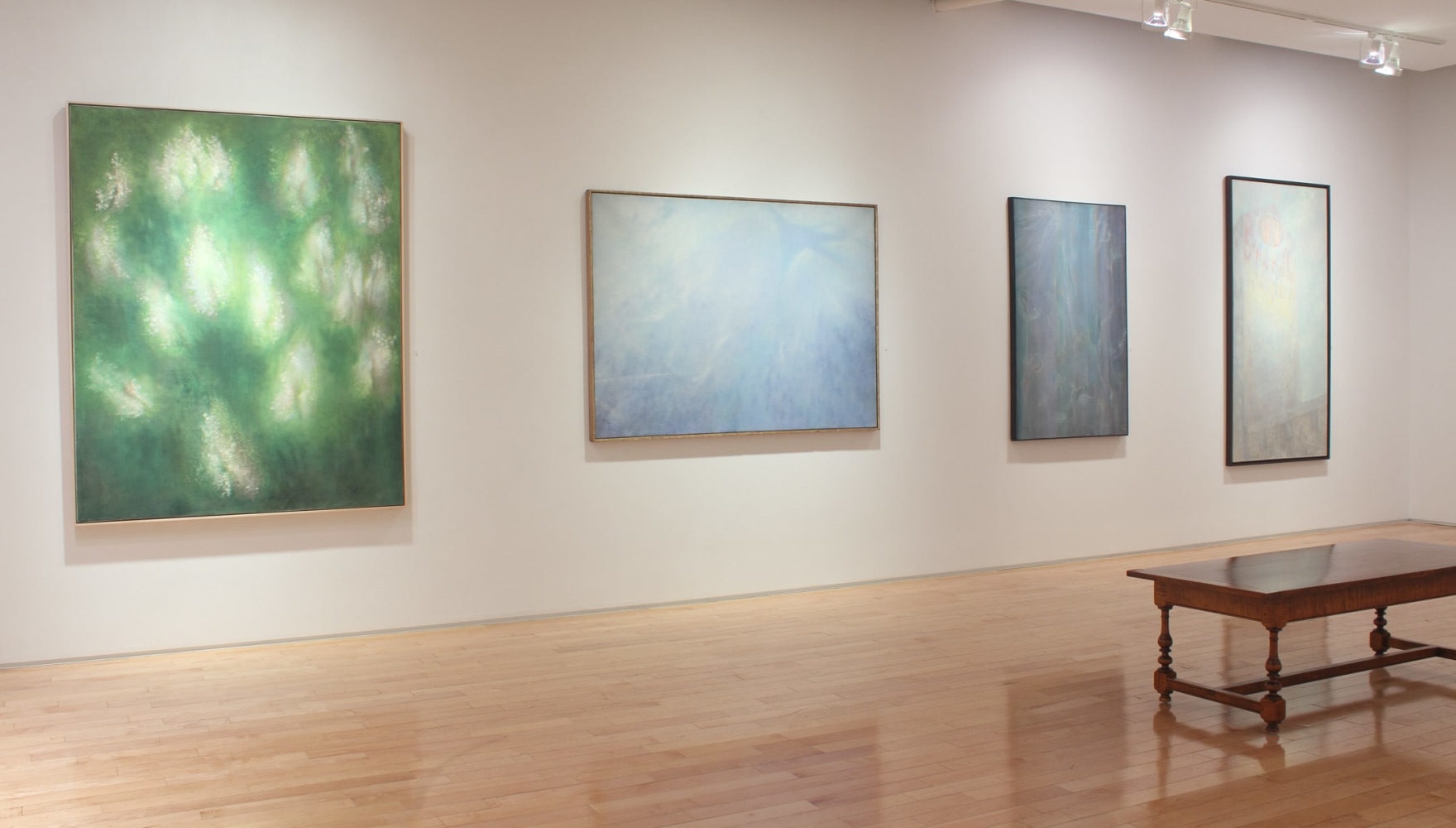 Photograph showing a view of an exhibition space with four large paintings hanging on a white wall