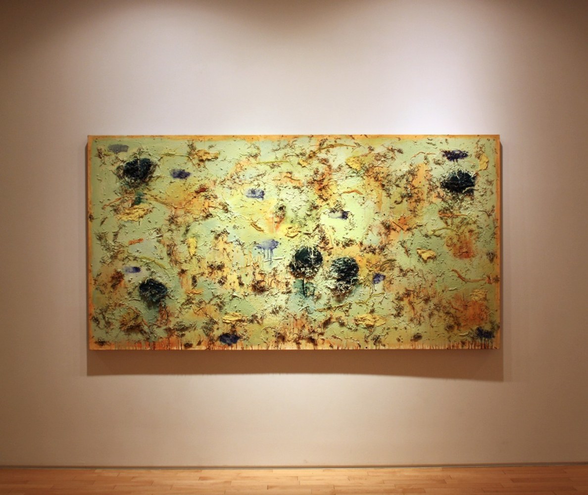 Photograph showing a view of an exhibition, with one large framed painting hanging on a white wall