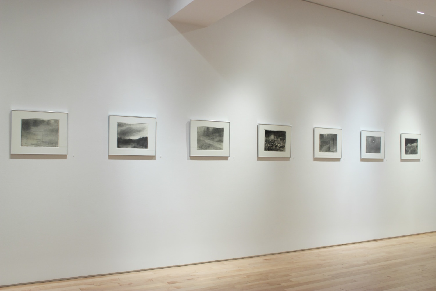 Photograph showing a view of an exhibition space with seven framed drawings hanging on a white wall