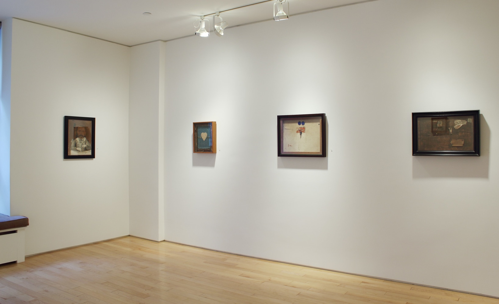 Photograph showing a corner view of an exhibition space with four paintings hanging on white walls