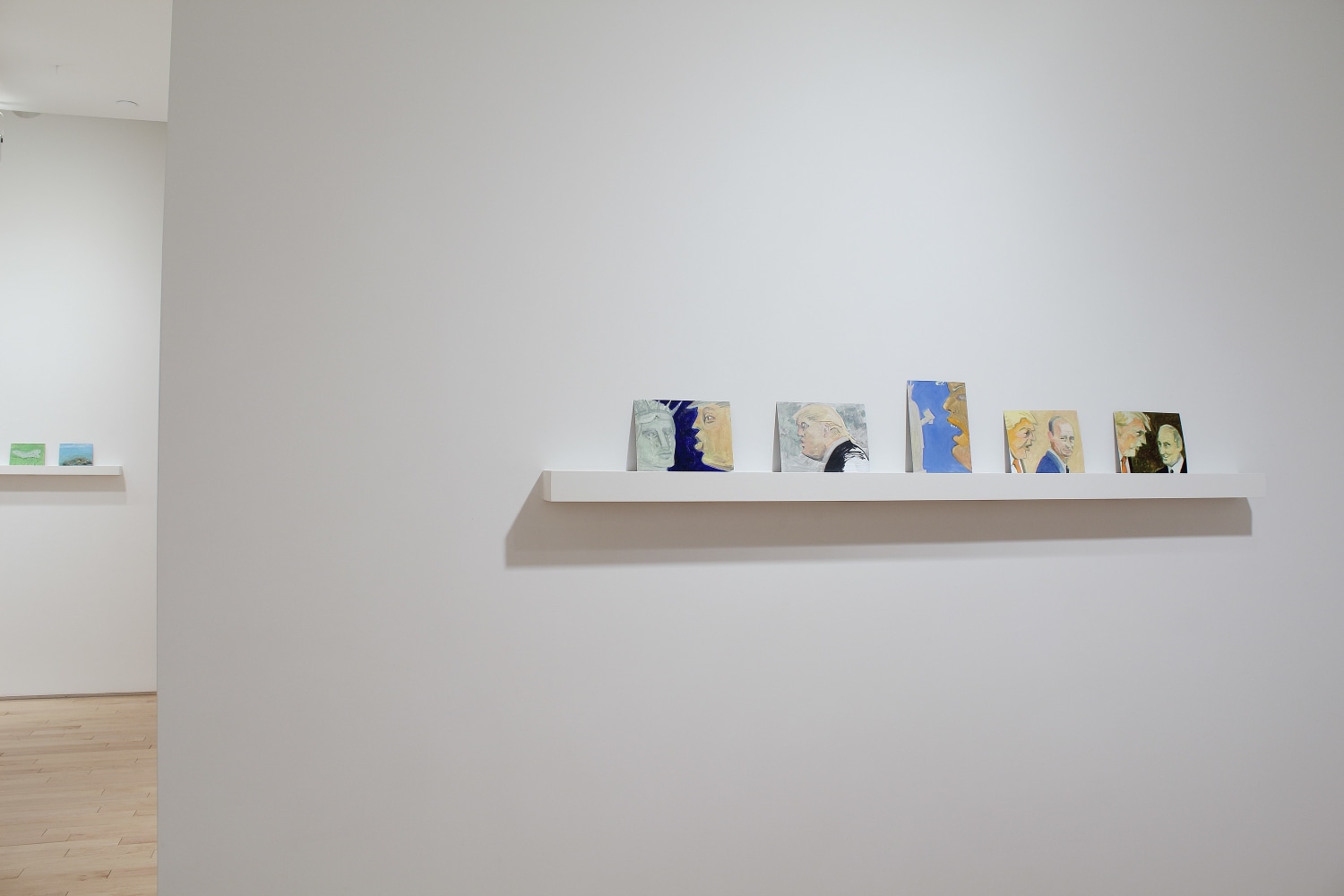Photograph showing a view of an exhibition space, with five small paintings on a shelf on a white wall