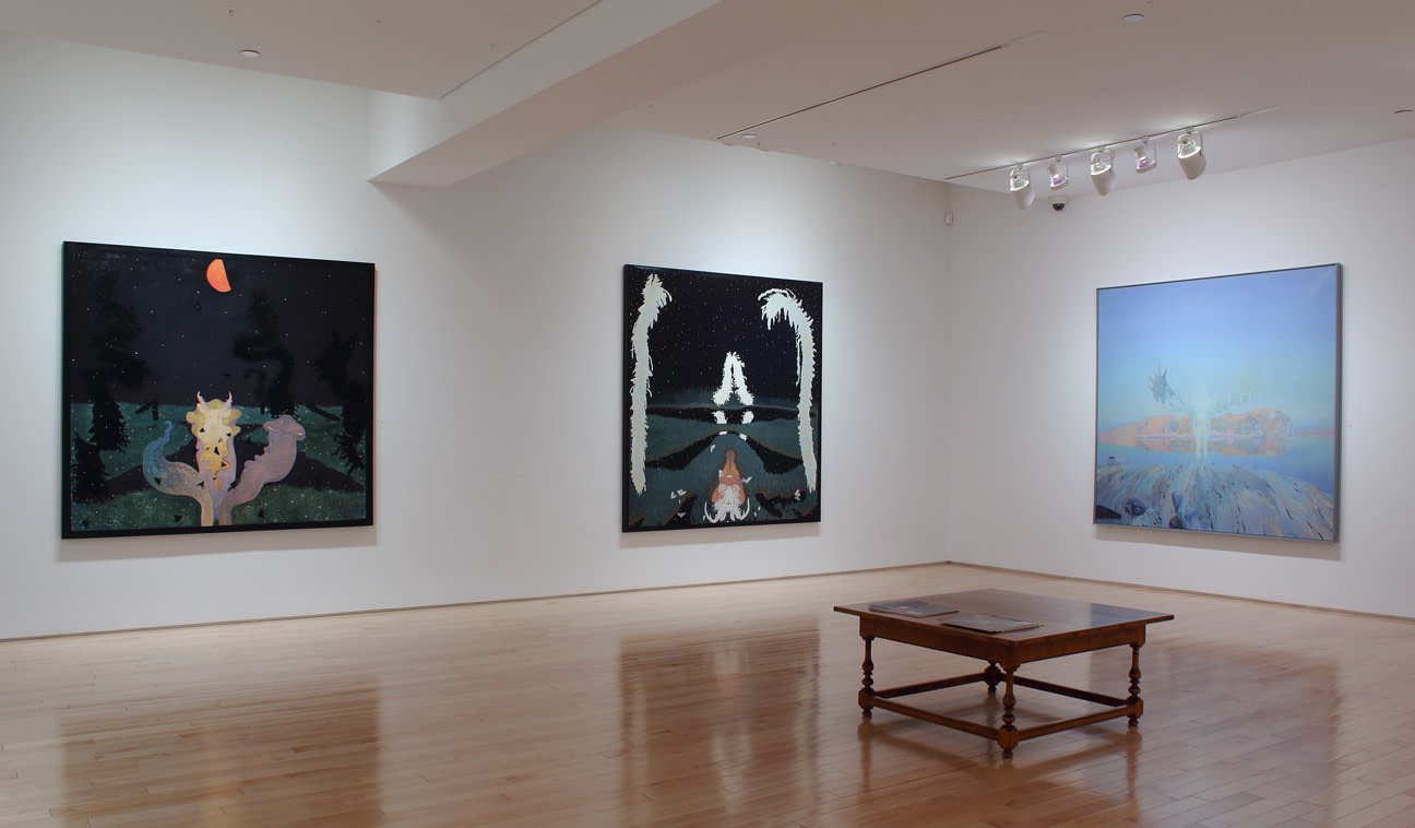 Photograph showing a corner view of an exhibition space with three paintings hanging on white walls