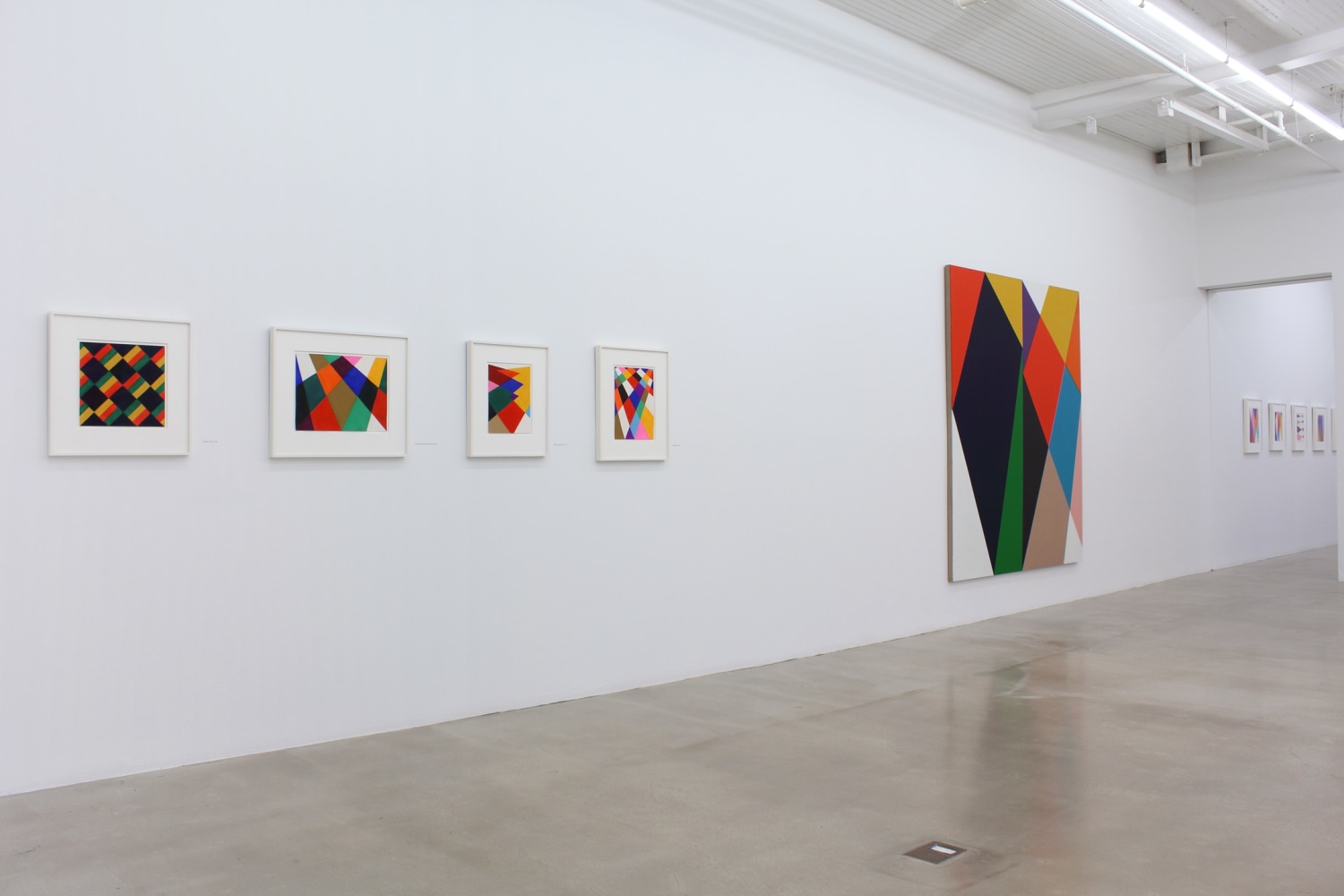 Photograph showing a view of an exhibition space, with eight paintings hanging on a white wall