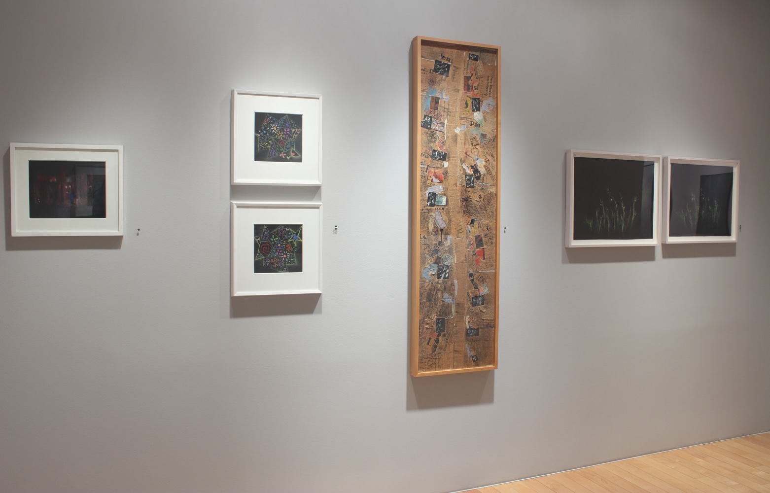 Photograph showing a view of an exhibition, with one large collage and five small framed drawings hanging on a grey wall