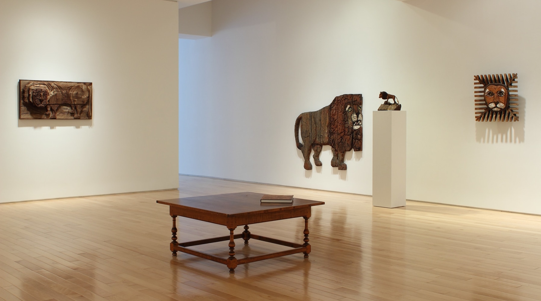 Photograph showing a corner view of an exhibition space, with three sculptures hanging on the walls, and a small sculpture on top of a pedestal