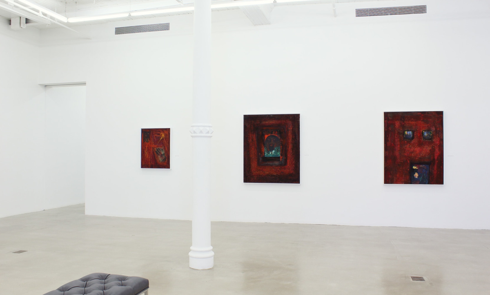 Photograph showing a view of an exhibition space, with three paintings hung on a white wall