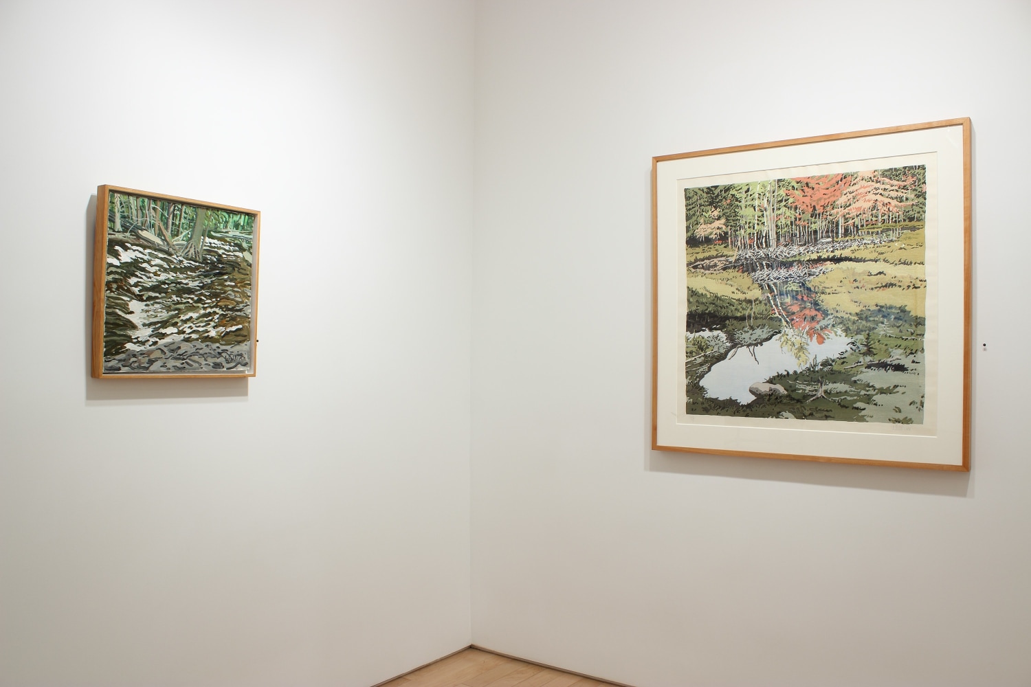 Photograph showing a corner view of an exhibition with two paintings hanging on white walls