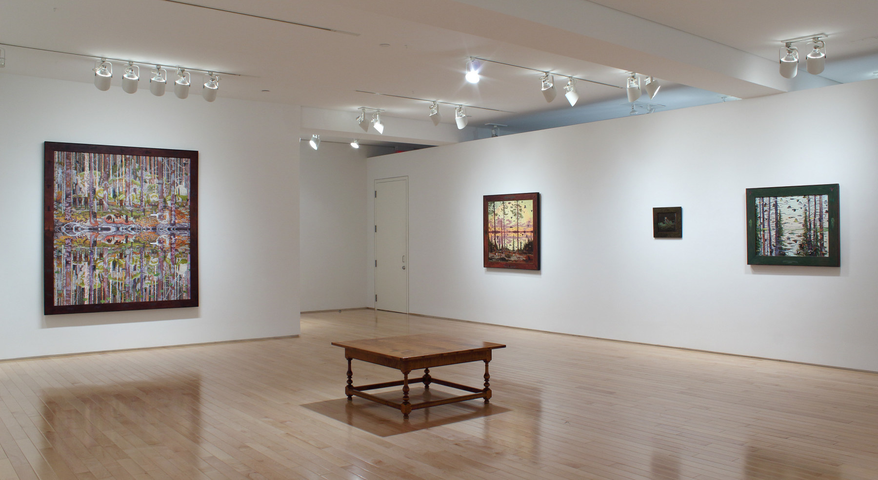 Photograph showing a corner view of an exhibition space, with four paintings hanging on white walls