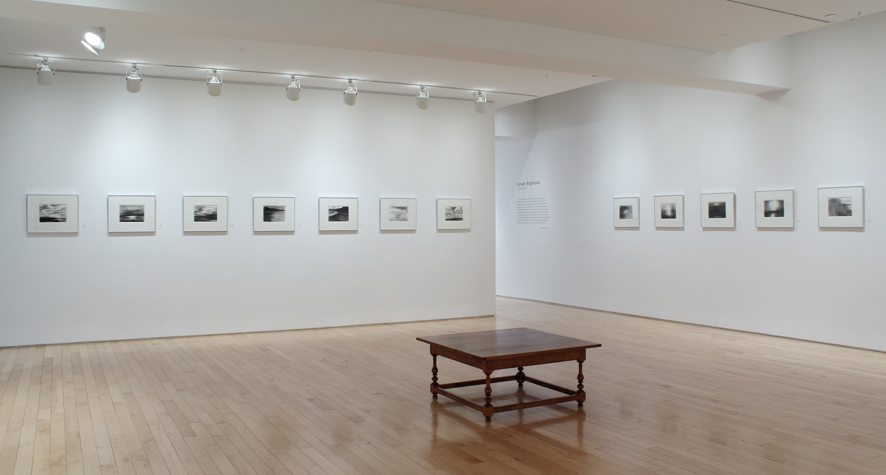 Photograph showing a corner view of an exhibition space, with twelve framed drawings hanging on white walls