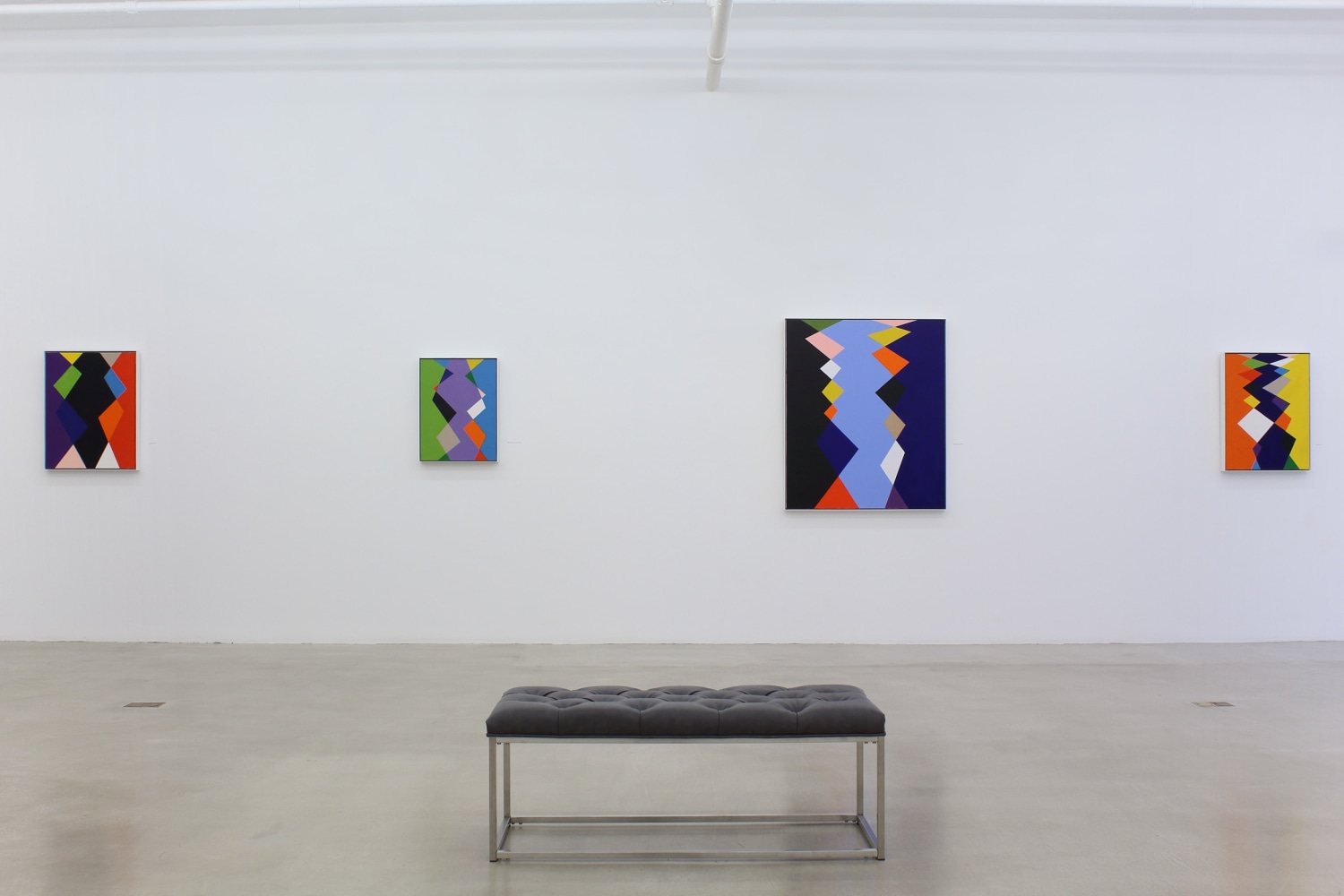 Photograph showing a view of an exhibition space, with four paintings hanging on a white wall