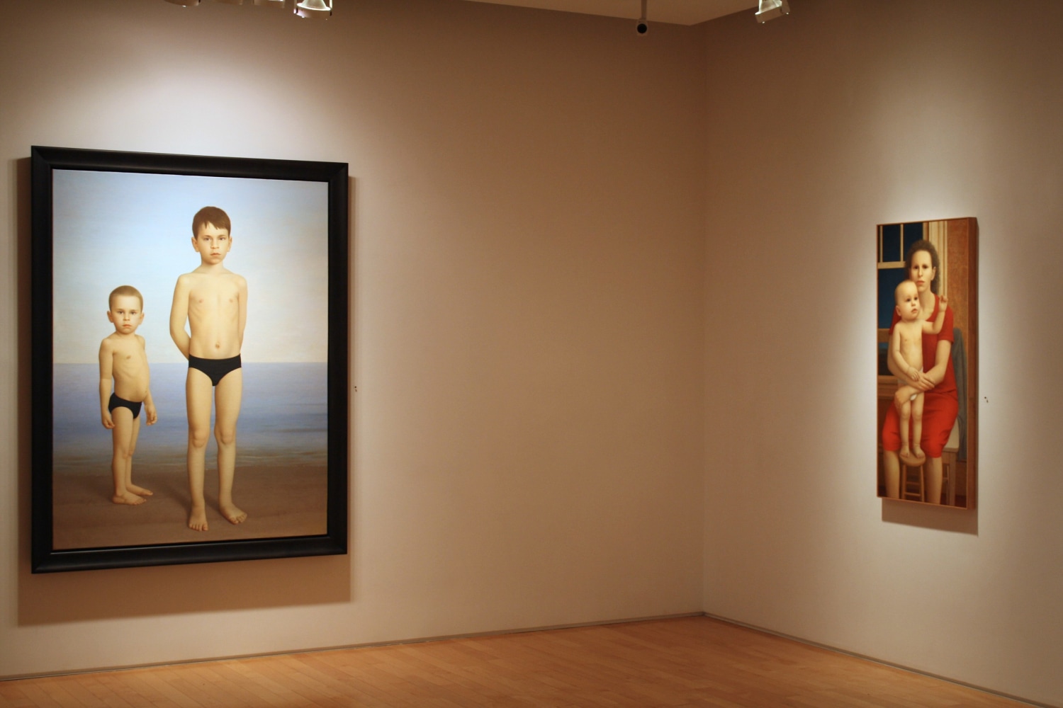 Photograph showing a corner view of an exhibition space, with two large framed paintings hanging on white walls