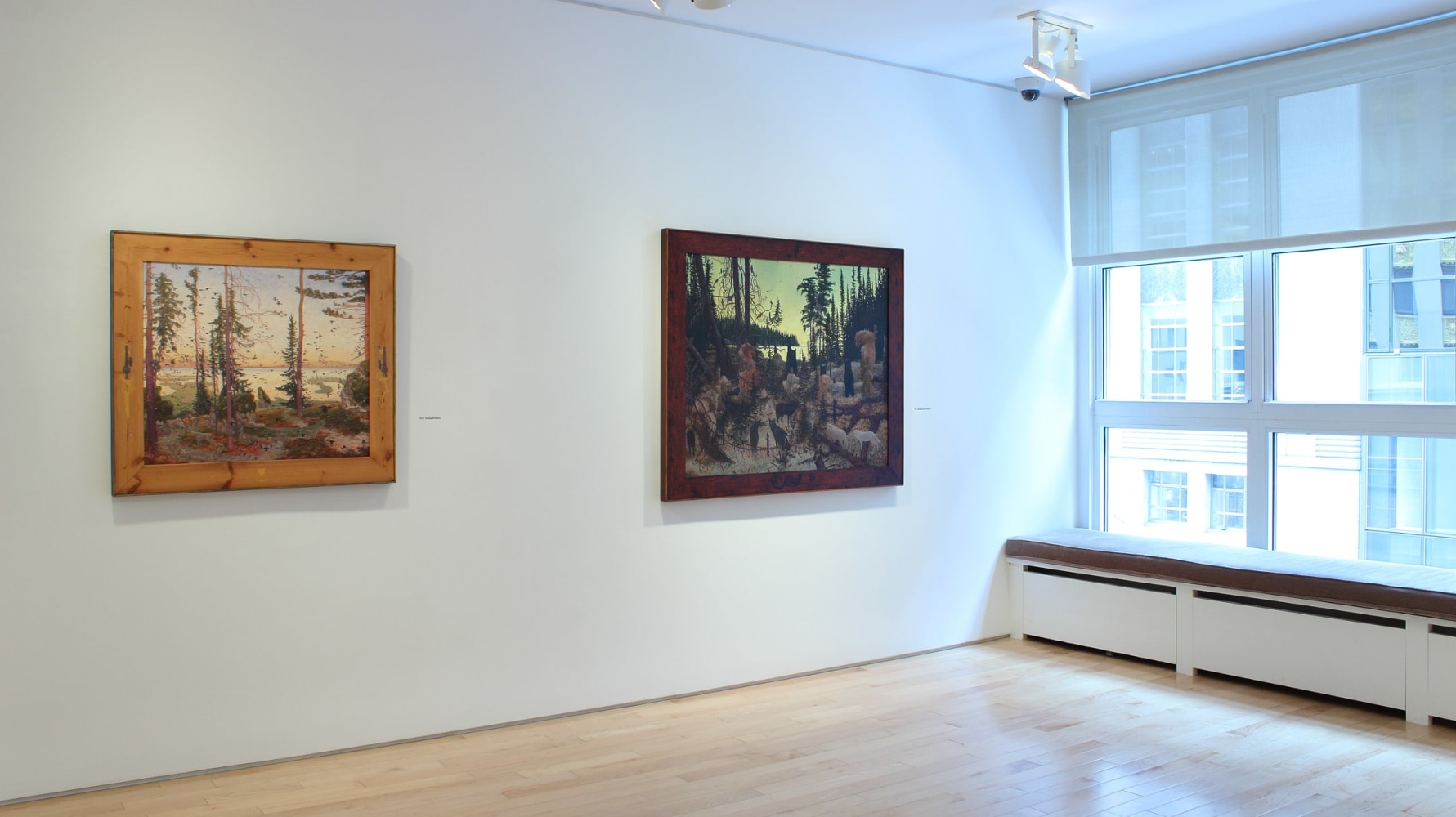 Photograph showing a view of an exhibition space, with two paintings hanging on a white wall