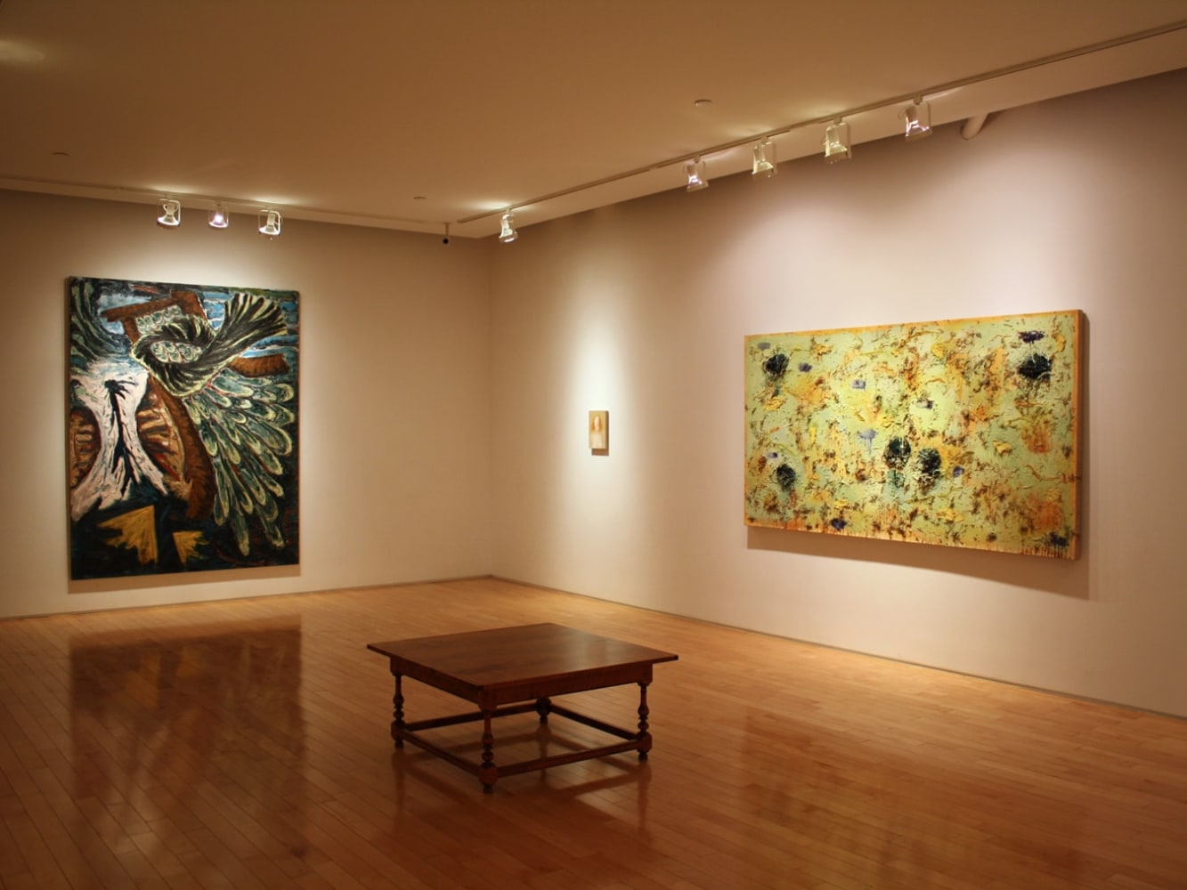 Photograph showing a corner view of an exhibition space, with two large framed paintings and one smaller framed painting hanging on white walls