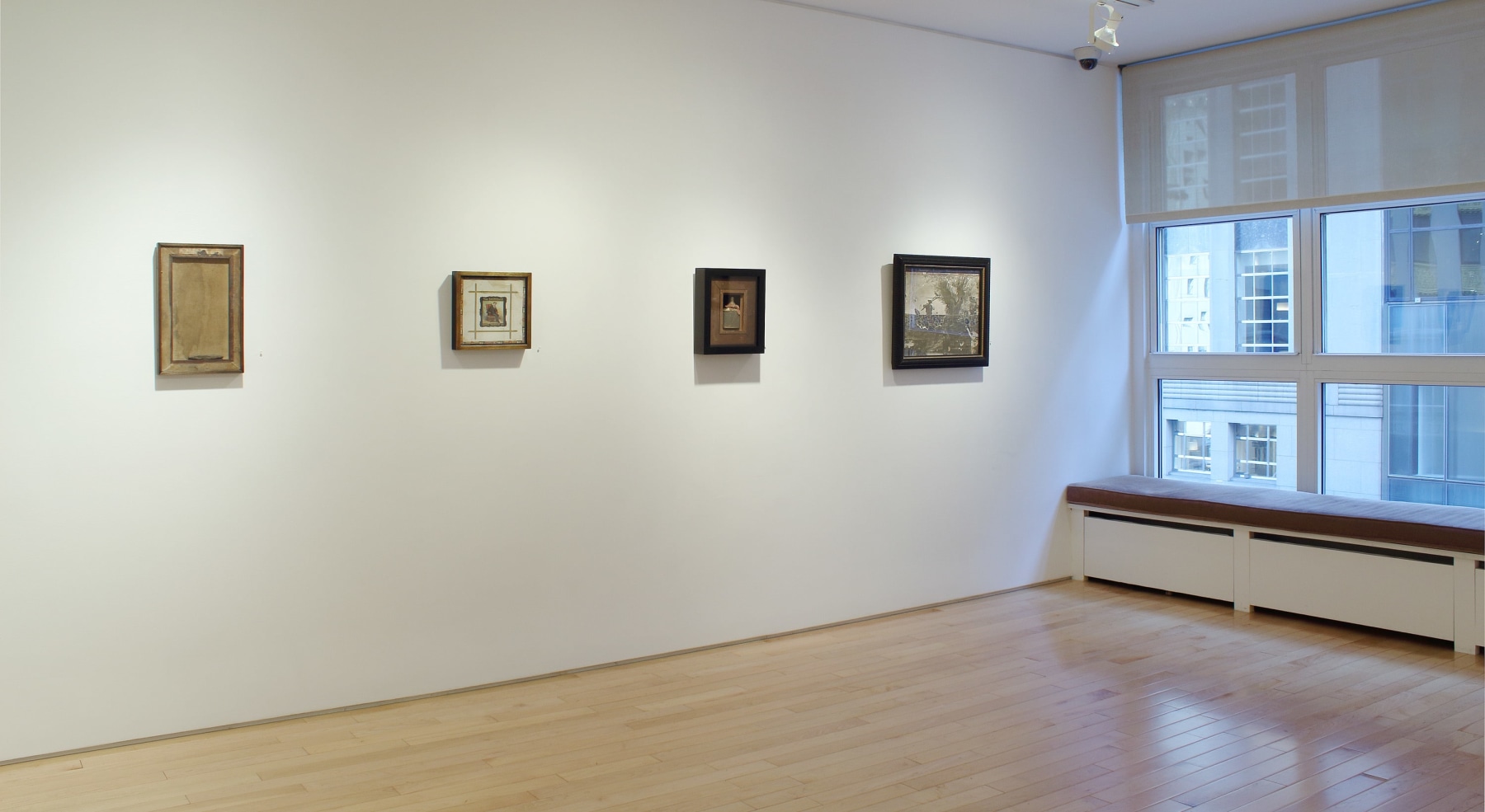 Photograph showing a view of an exhibition space with four paintings hanging on a white wall
