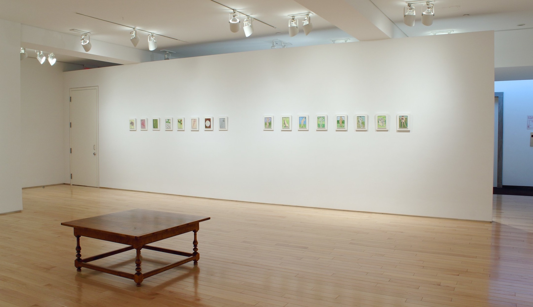 Photograph showing a view of an exhibition space, with a row of sixteen small paintings hung on a white wall