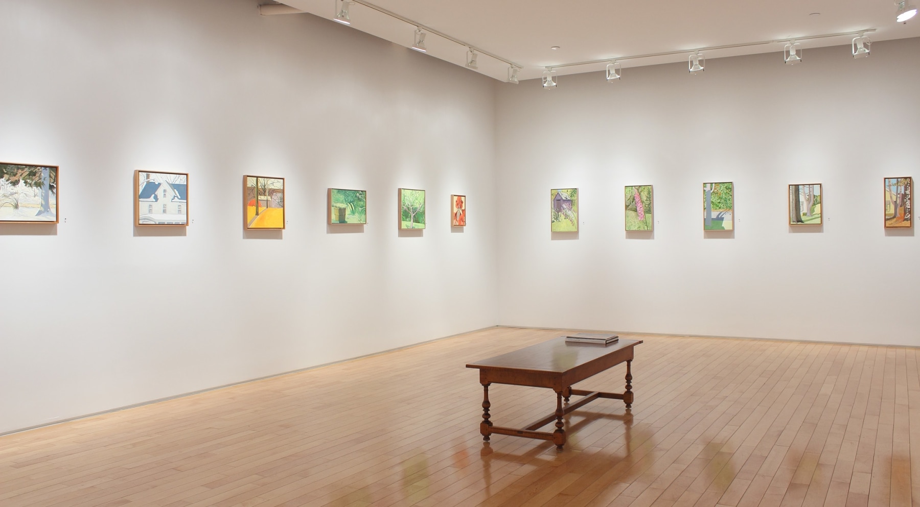 Photograph showing a corner view of an exhibition space with eleven small paintings hanging on white walls