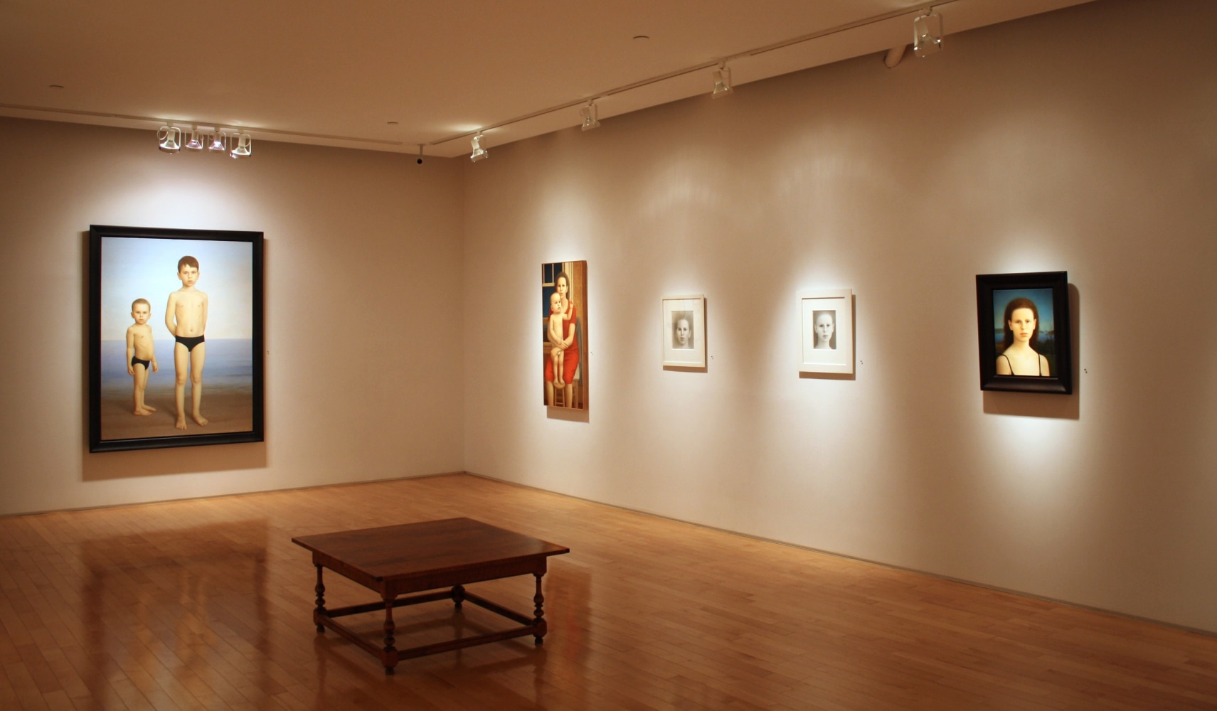 Photograph showing a corner view of an exhibition space, with three framed paintings and two small framed drawings hanging on white walls