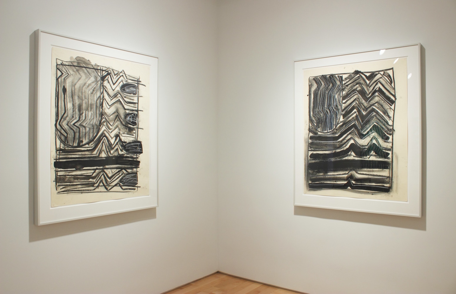 Photograph showing a corner view of an exhibition space, with two framed drawings hanging on white walls