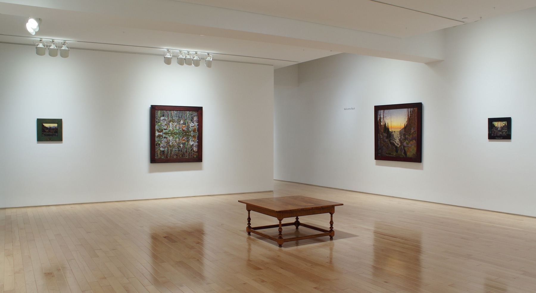 Photograph showing a corner view of an exhibition space, with four paintings hanging on white walls