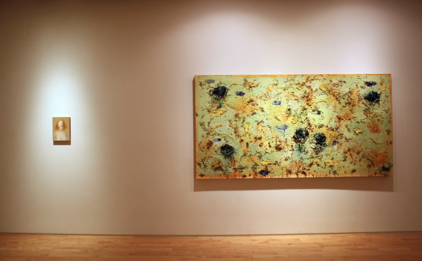 Photograph showing a view of an exhibition, with one large framed painting and one small framed painting hanging on a white wall