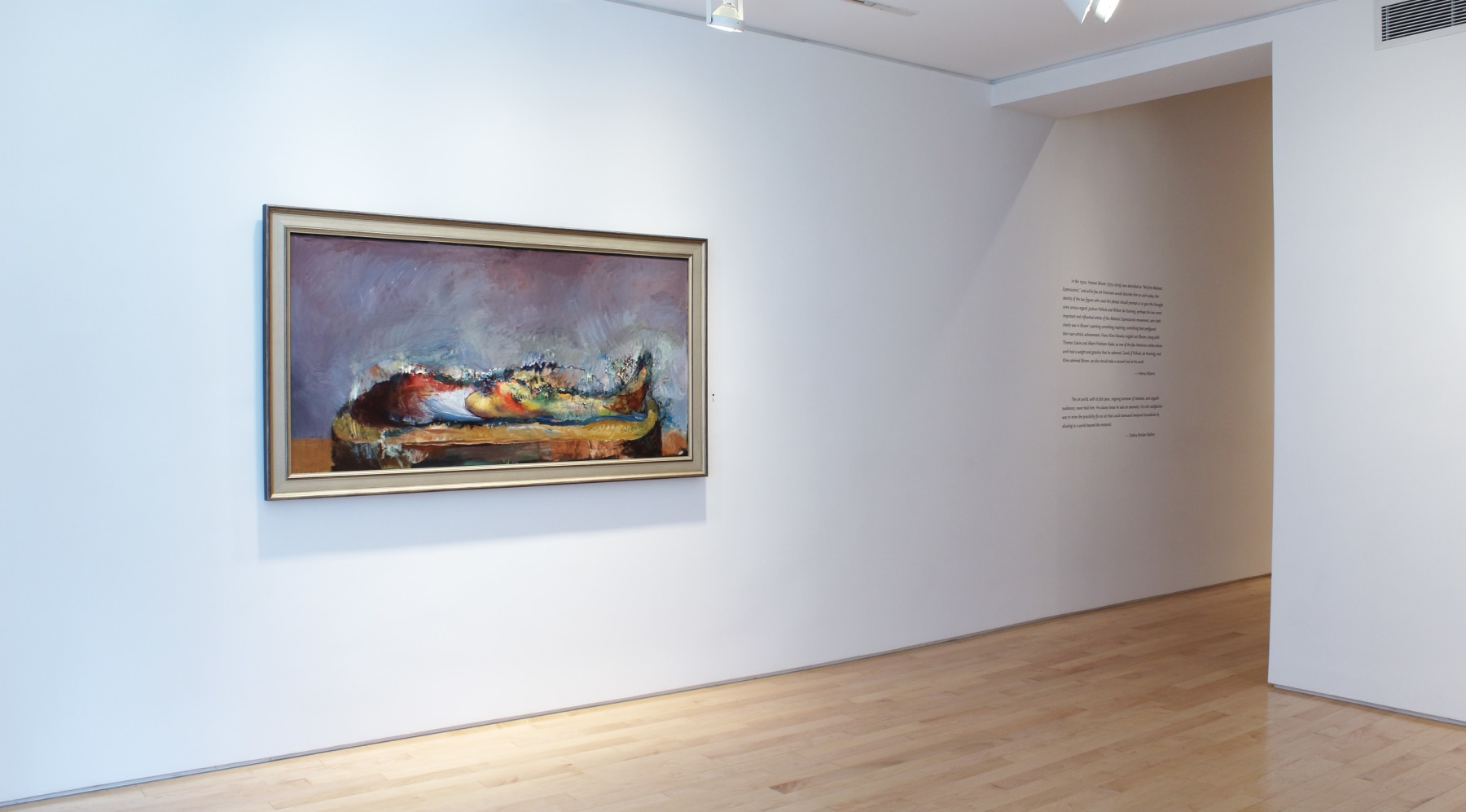 Photograph showing a corner view of an exhibition space with one painting hanging on white walls