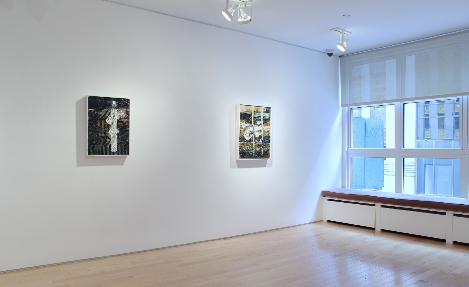 Photograph showing a view of an exhibition space, with two paintings hanging on a white wall