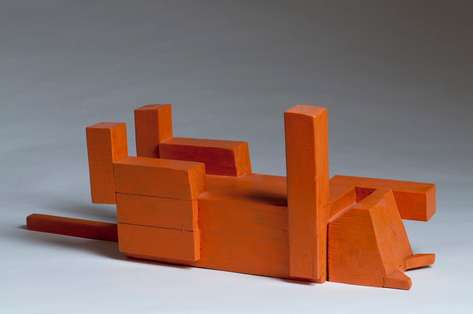 Abstracted sculpture of a cat lying on its back created from blocks of wood, painted orange