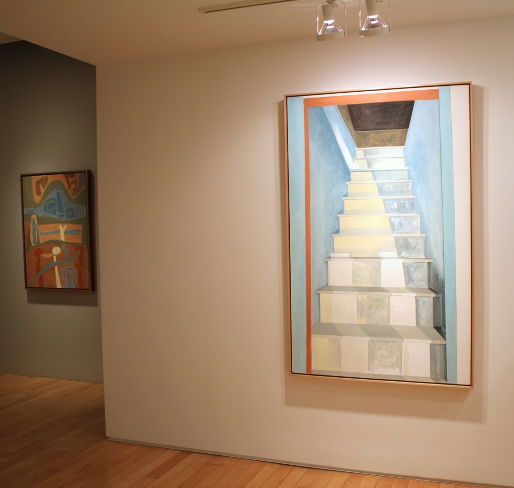 Photograph showing a view of an exhibition, with two framed paintings hanging on the walls