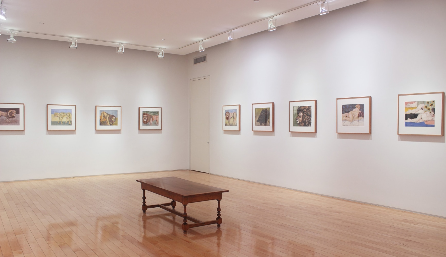 Photograph showing a corner view of an exhibition space with nine framed paintings hanging on white walls
