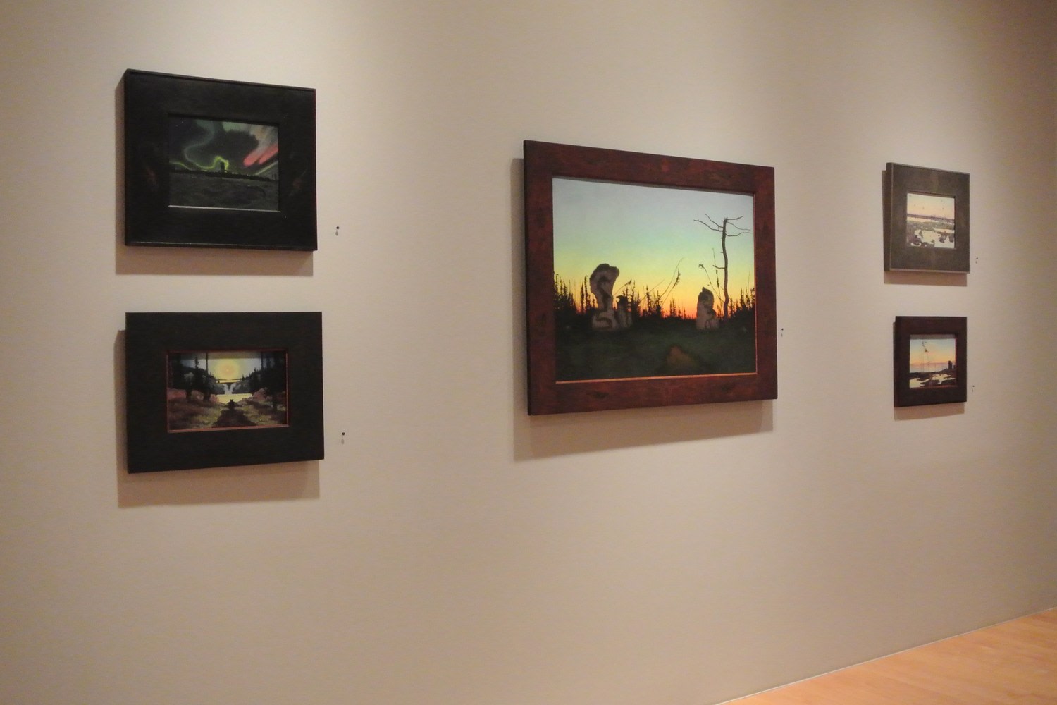 Photograph showing a view of an exhibition space, with five framed paintings hanging on a grey wall