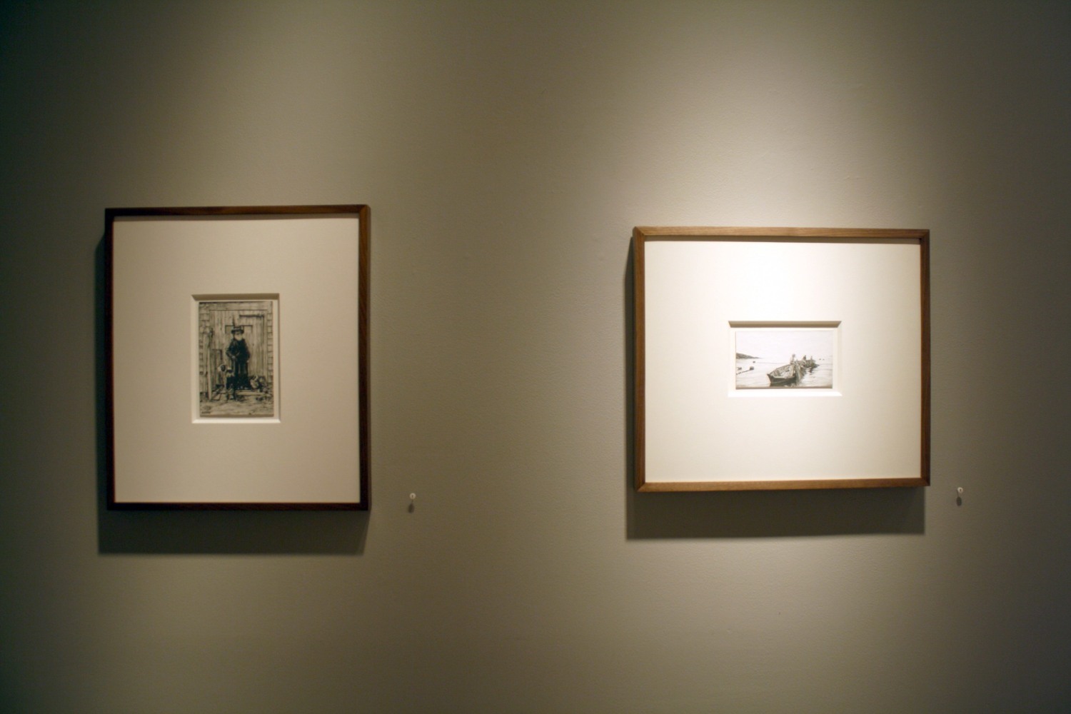 Photograph showing a view of an exhibition, with two small framed drawings hanging on a grey wall