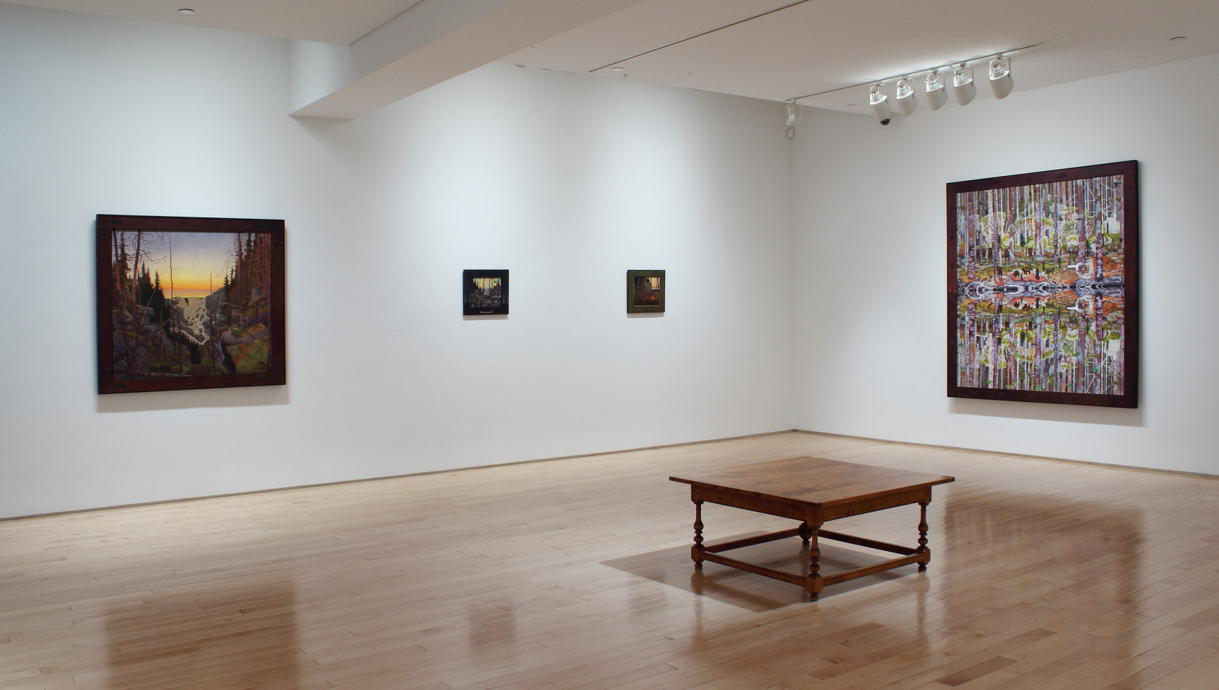 Photograph of a corner view of an exhibition space, with four paintings hung on white walls