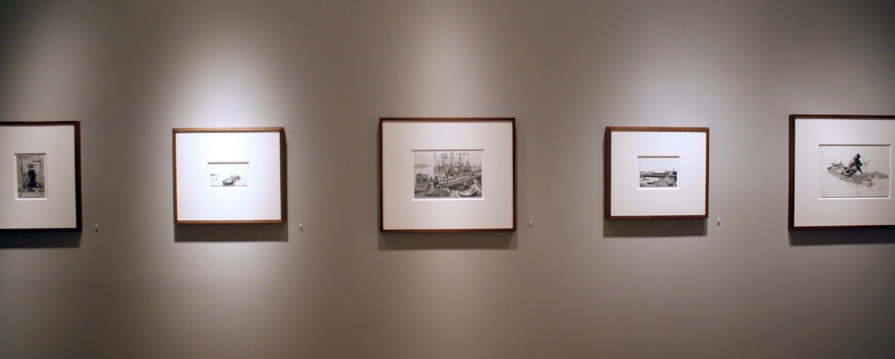Photograph showing a view of an exhibition, with five small framed drawings hanging on a grey wall