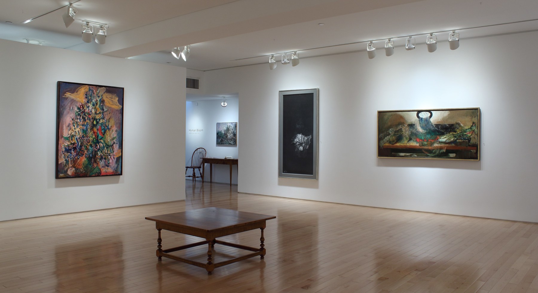 Photograph showing a corner view of an exhibition space with four paintings hanging on white walls
